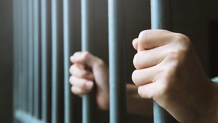A person holding onto the bars of their jail cell.