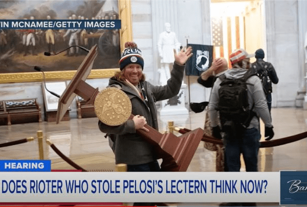 Adam Johnson wearing a beanie and waving while carrying Pelosi's podium out of a building