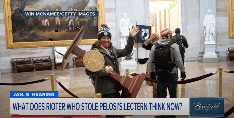 Adam Johnson wearing a beanie and waving while carrying Pelosi's podium out of a building